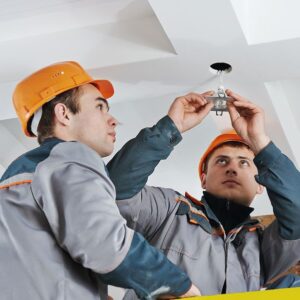 electrician worker in uniform installing or replacing spot light lamp into ceiling